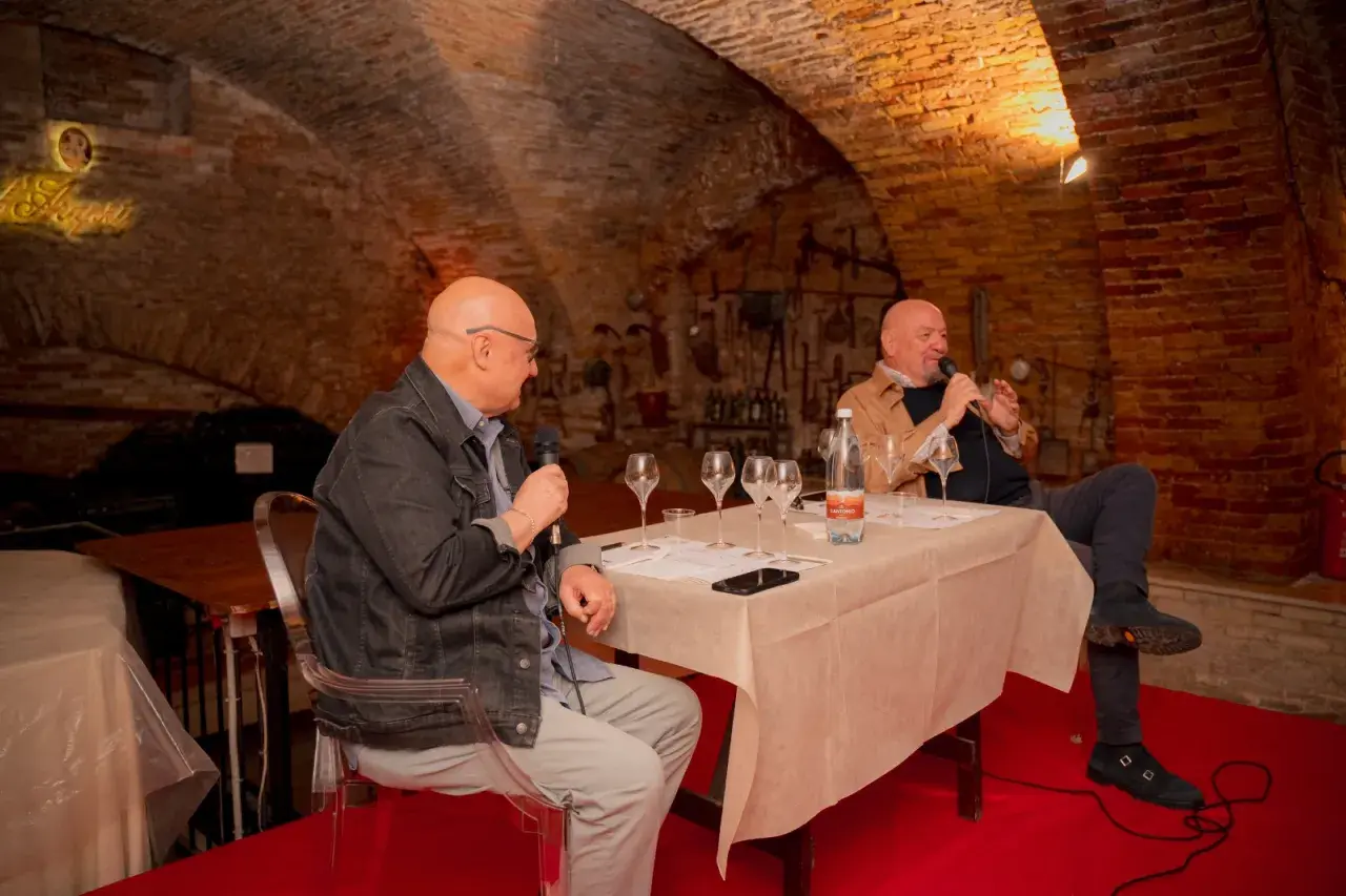 Due uomini discutono del metodo champagne in una cantina storica, con bicchieri da degustazione pronti.