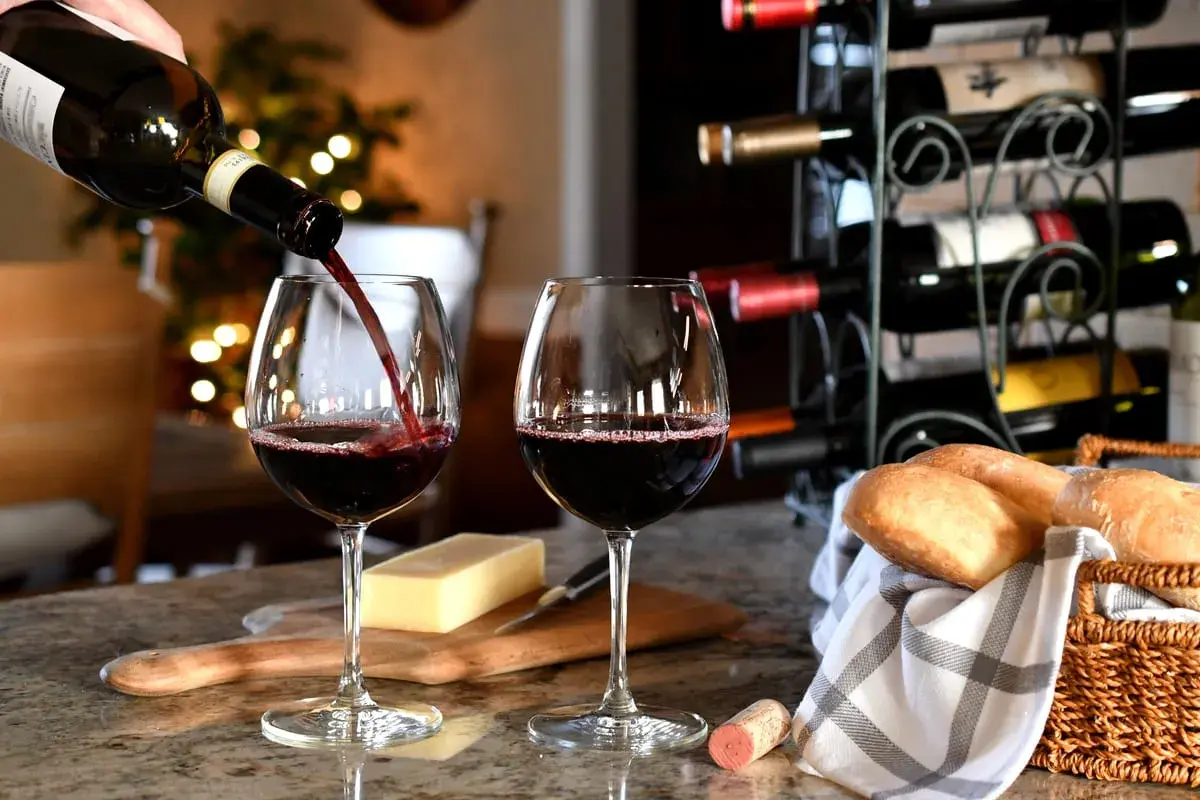 Versare vino rosso in un bicchiere, con pane e formaggio. Un promemoria su come conservare il vino rosso per gustarlo al meglio.