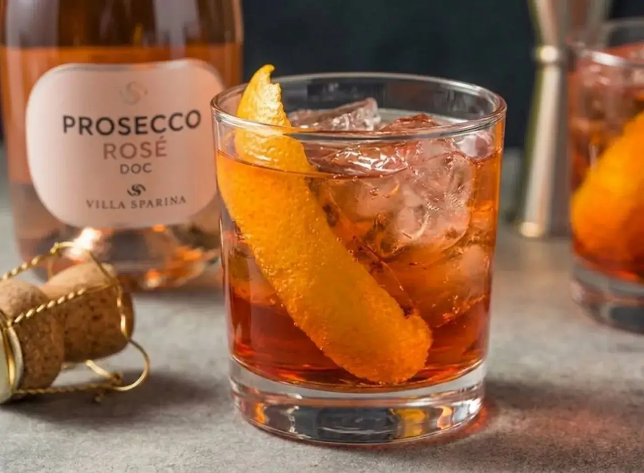 Un Negroni Sbagliato con prosecco, ghiaccio e scorza d'arancia. Accanto, una bottiglia di Prosecco Rosé DOC.