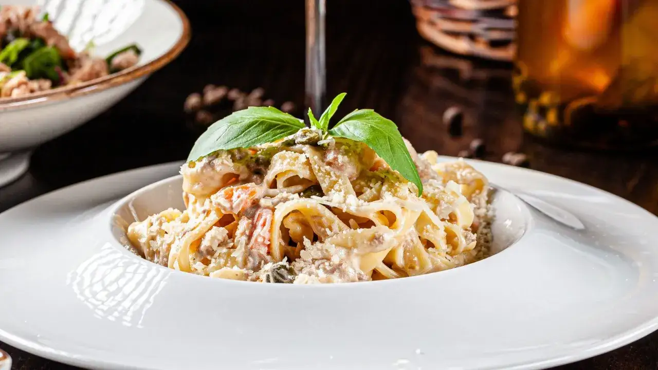 Un piatto di pasta con ricotta, condita con erbe fresche e parmigiano, servita in una ciotola bianca.