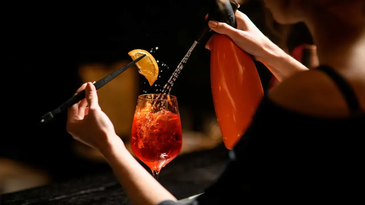 Un bicchiere di Aperol Spritz, con una fetta d'arancia e spruzzi d'acqua, pronto per la tua ricetta pirlo bianco.