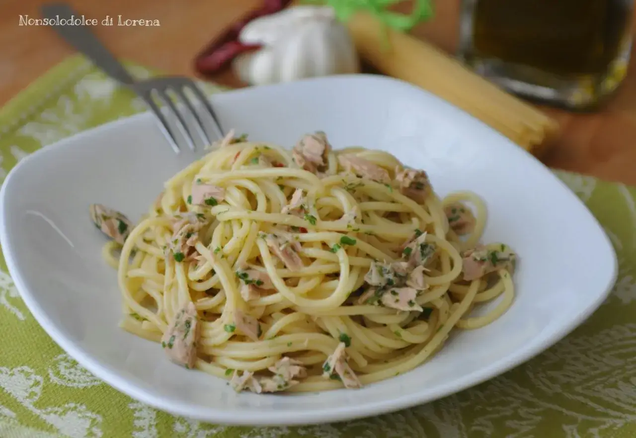 Un piatto invitante di spaghetti con tonno e limone, guarnito con prezzemolo fresco. Sullo sfondo, ingredienti per un pasto gustoso.