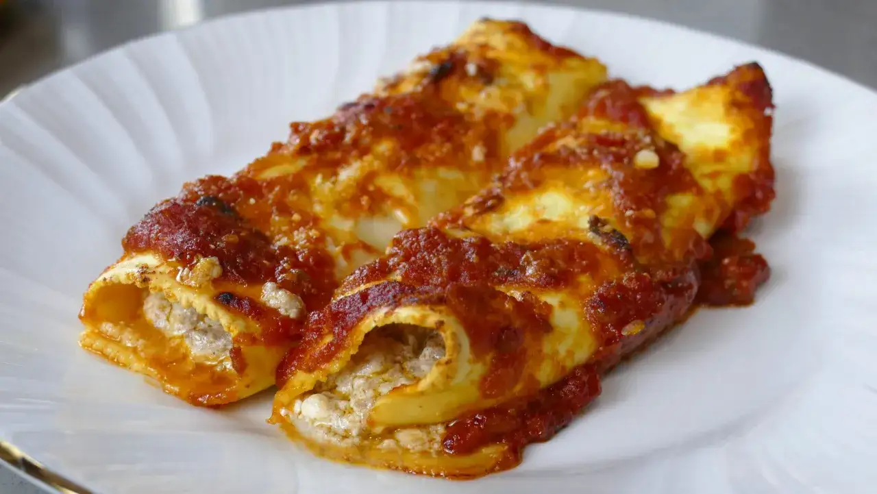Due cannelloni ripieni, ricoperti di sugo rosso e formaggio grattugiato, serviti su un piatto bianco.