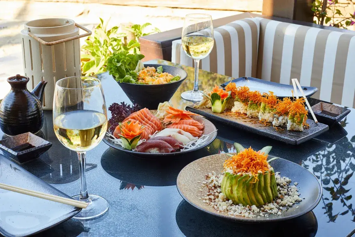 Un perfetto abbinamento vino sushi: sashimi, roll e avocado fresco, accompagnati da calici di vino bianco, su un tavolo all'aperto.