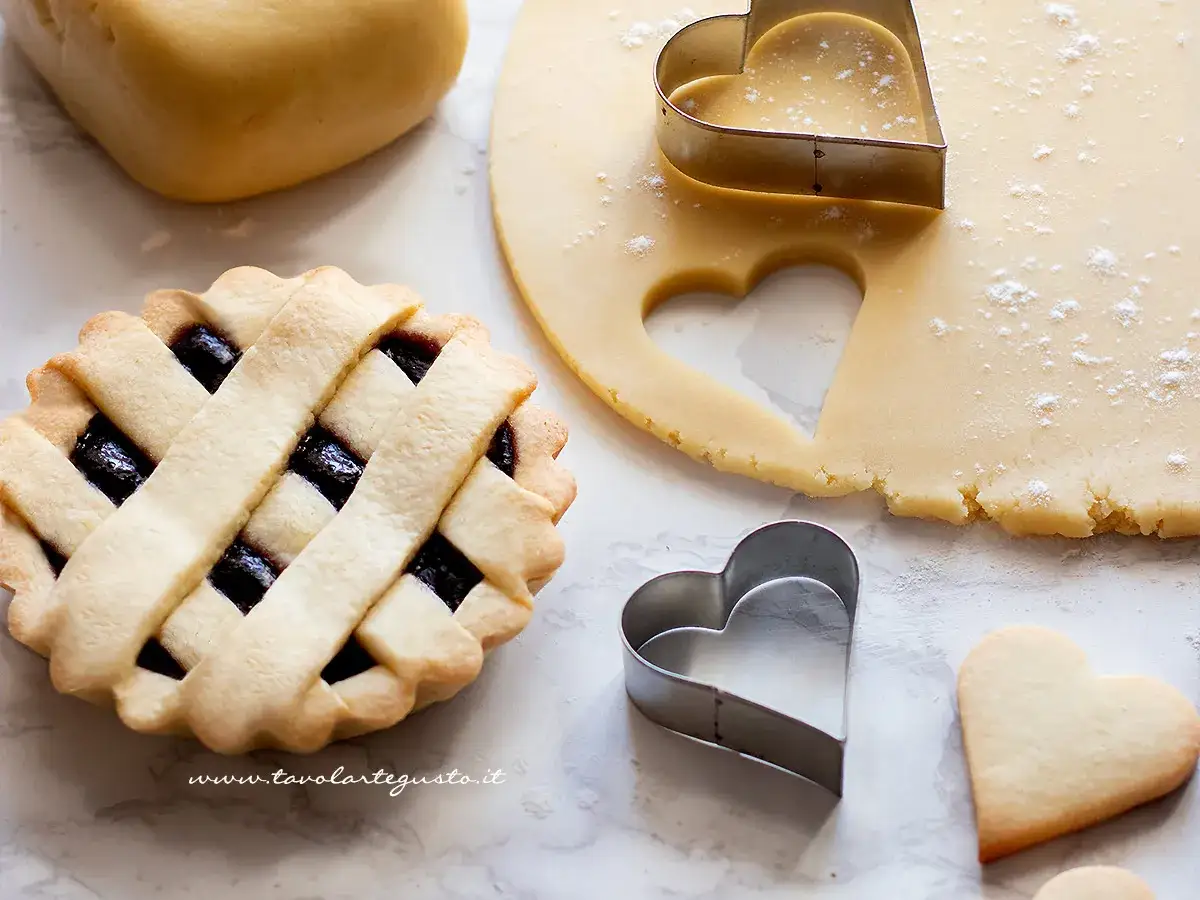 Preparazione di crostatine con pasta frolla e marmellata. Stesa di pasta frolla, formine a cuore e una crostatina pronta.