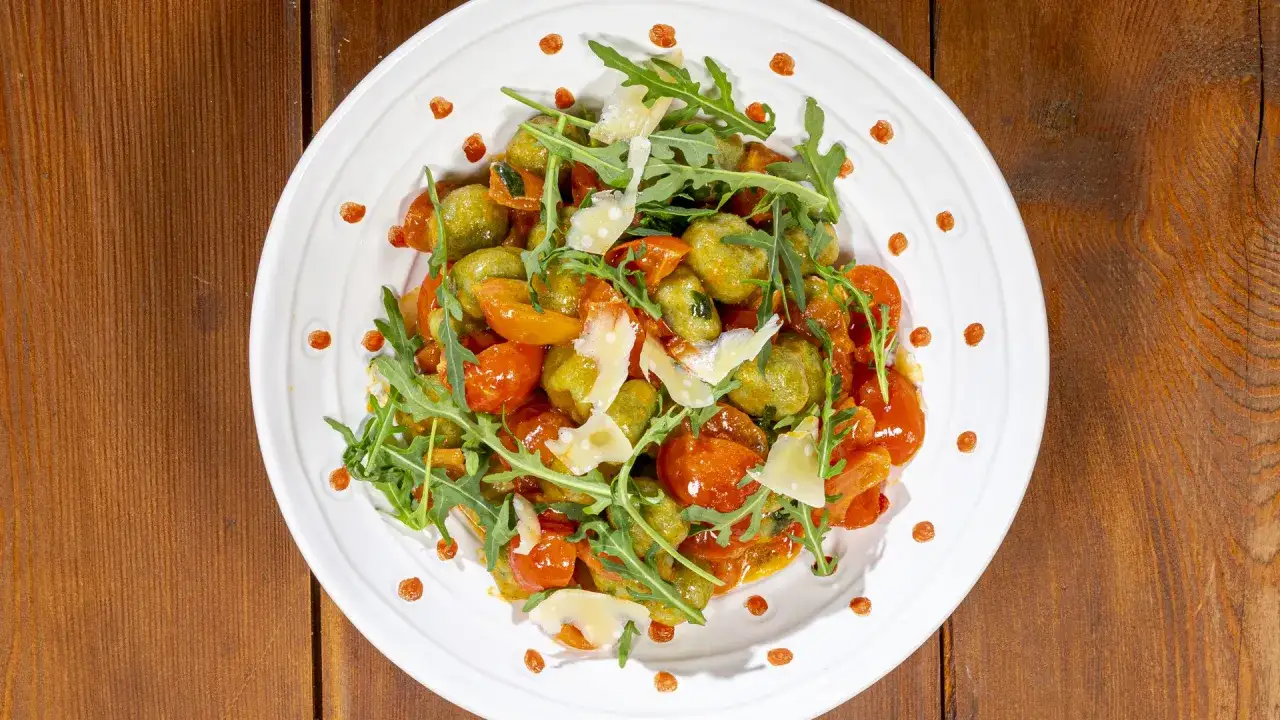Gnocchi di zucchine con pomodorini, rucola e scaglie di parmigiano, un piatto colorato e gustoso.