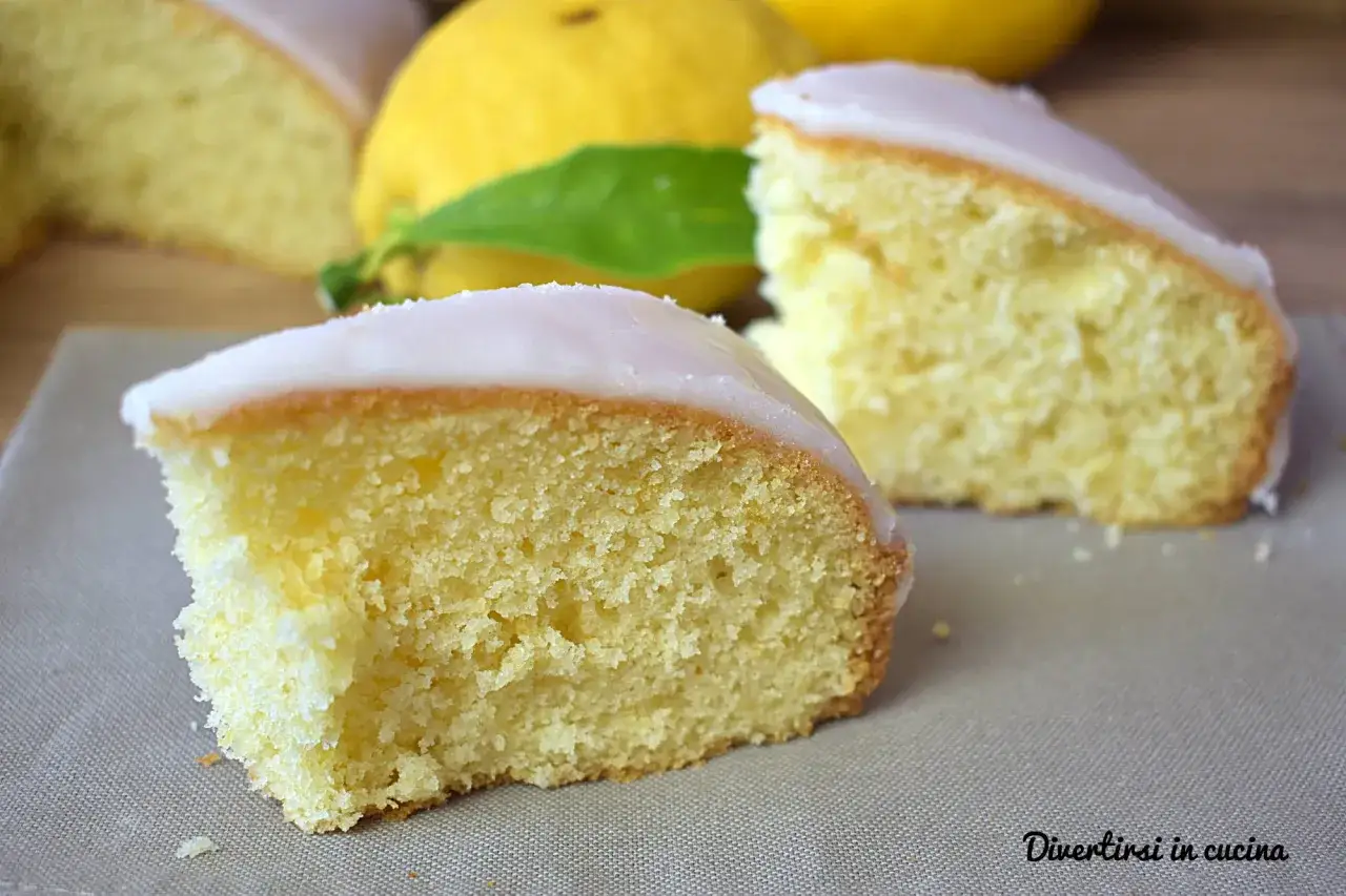 Fette di torta al limone soffice e profumata, con glassa bianca e limoni freschi sullo sfondo.