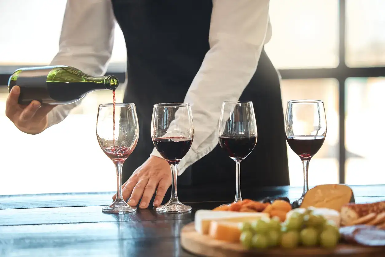 Un sommelier versa vino rosso in un calice, mostrando cosa fa un sommelier: un'arte di degustazione e abbinamento con formaggi e frutta.