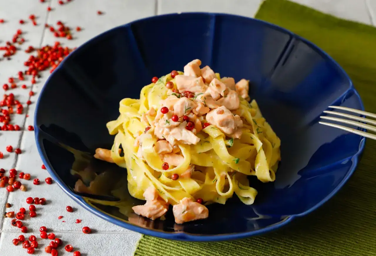 Un piatto di pasta panna e salmone, guarnito con pepe rosa e aneto, su un piatto blu.