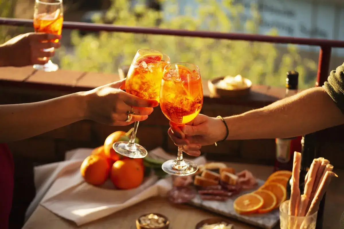 Un brindisi con Spritz, il vero significato dell'aperitivo: relax, amici e sapori italiani. Arance, salumi e stuzzichini completano la scena.