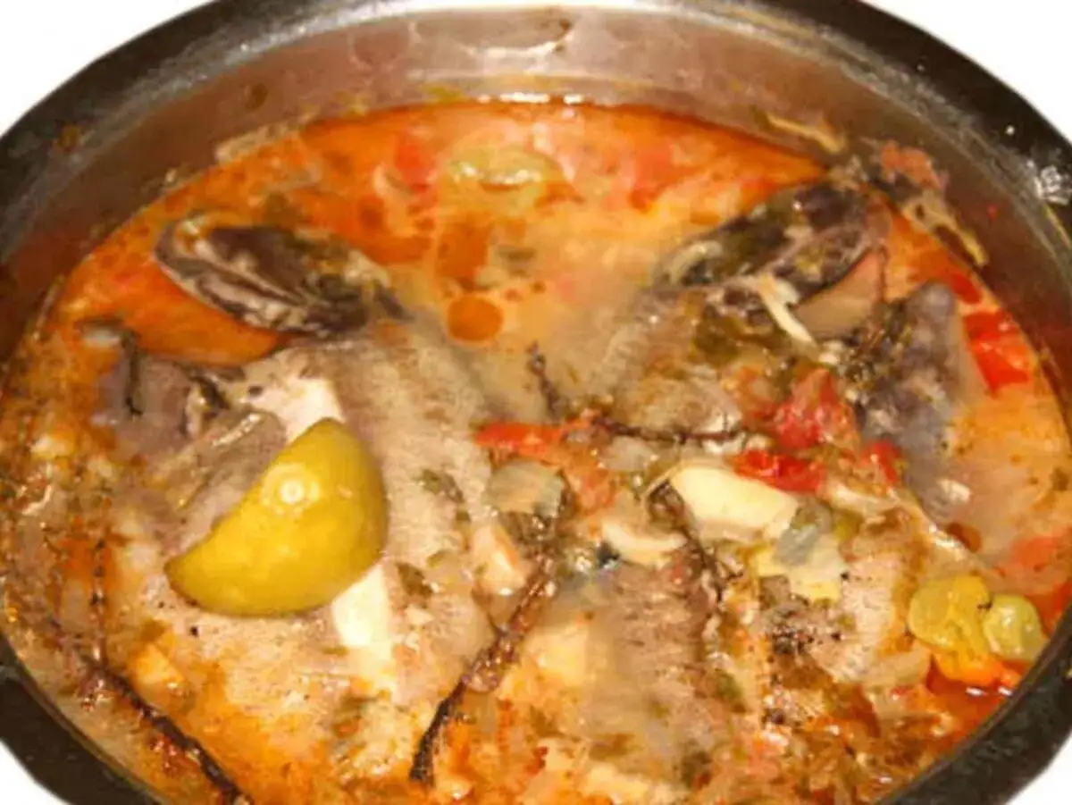 Un fumetto di pesce in umido, con pomodoro, limone e spezie, servito in una pentola.