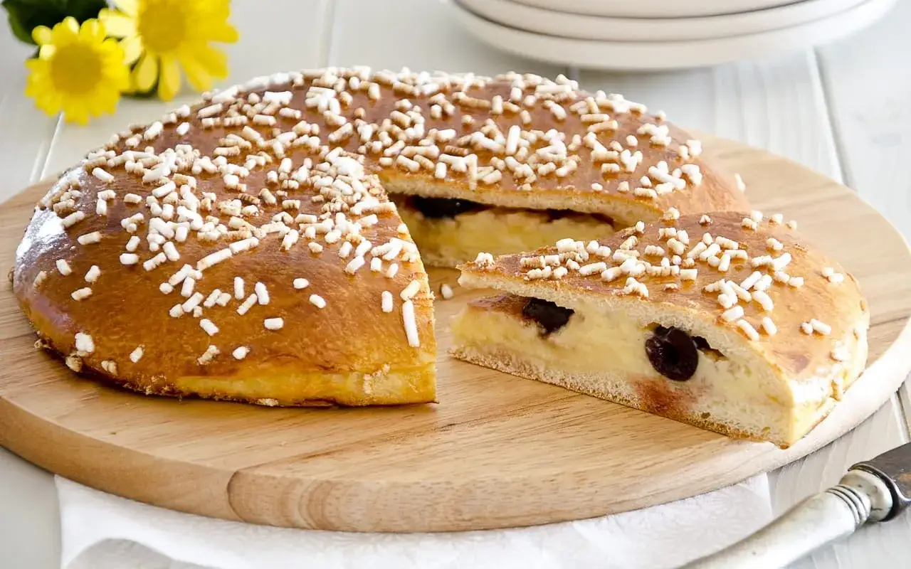 Deliziosa polacca aversana con crema pasticcera e ciliegie, cosparsa di zuccherini, su tagliere di legno.