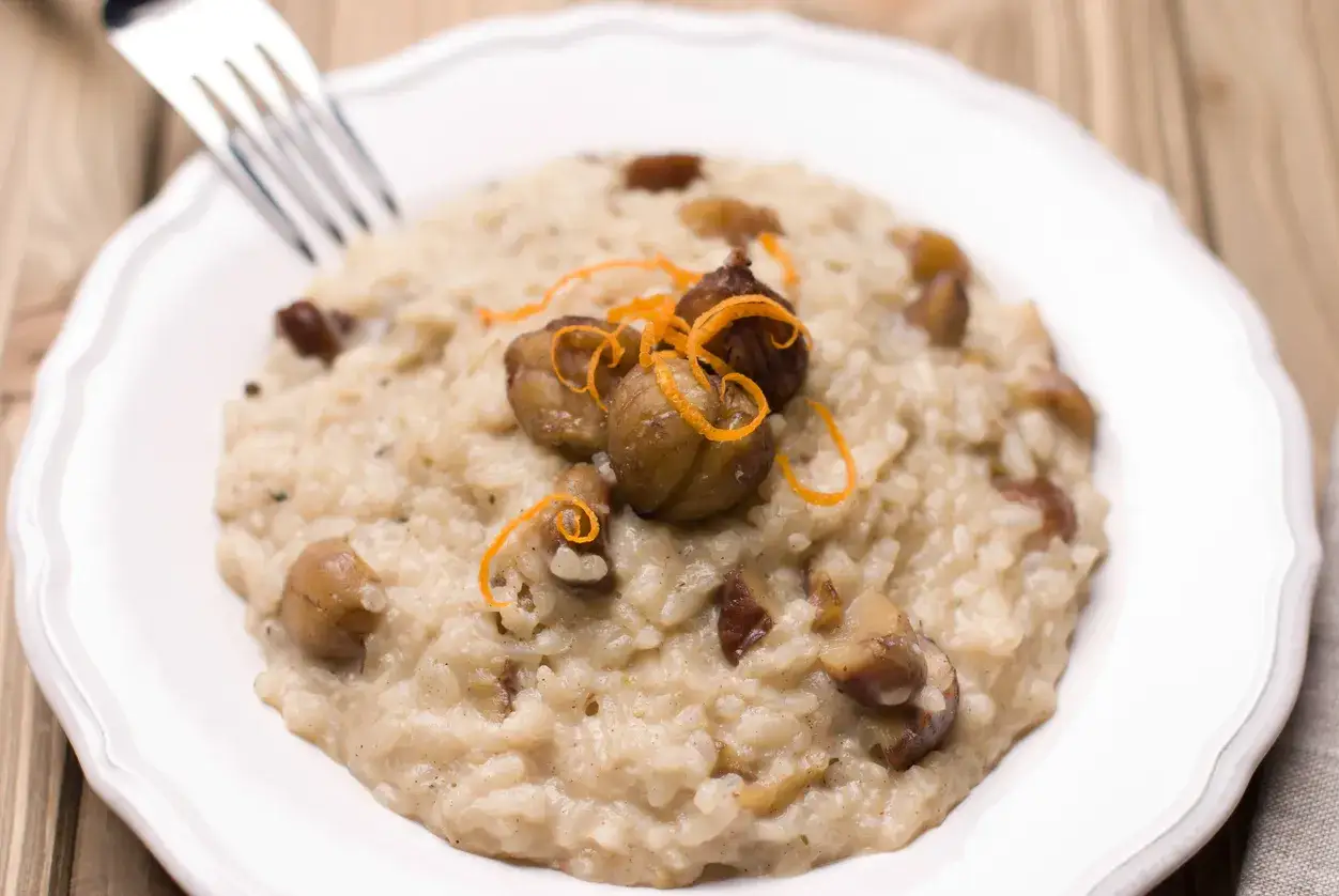 Risotto cremoso con castagne e gorgonzola, guarnito con scorza d'arancia. Un piatto autunnale invitante.