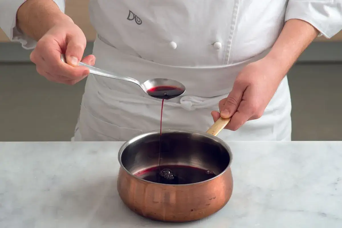 Chef versa un cucchiaio di riduzione di vino rosso in una pentola di rame.