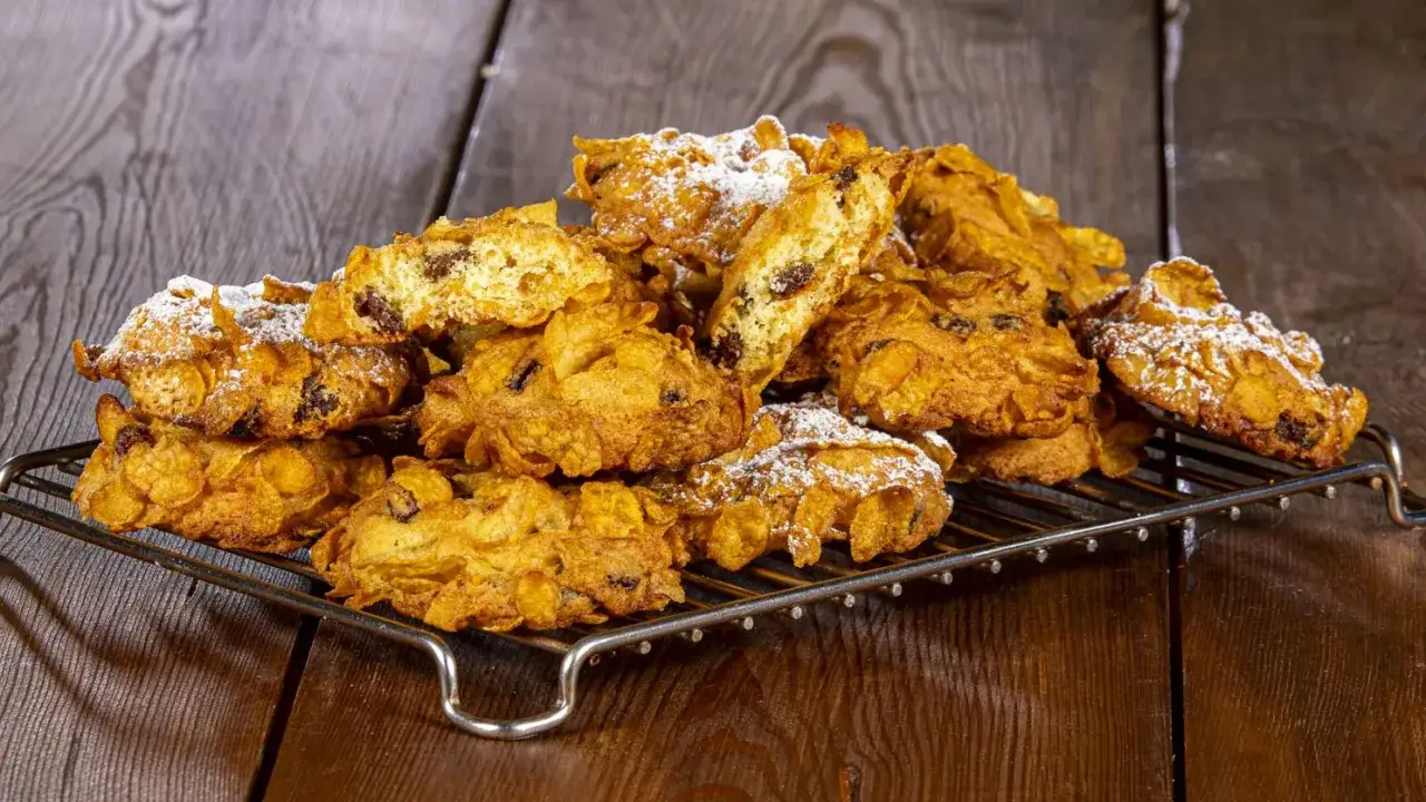 Un mucchio di croccanti biscotti, simili a rose del deserto, ricoperti di zucchero a velo, su una griglia metallica.