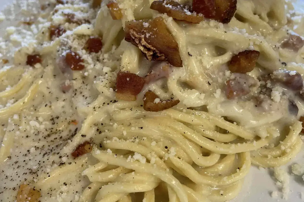 Spaghetti cremosi con guanciale croccante e pecorino romano grattugiato, un classico della cucina romana.