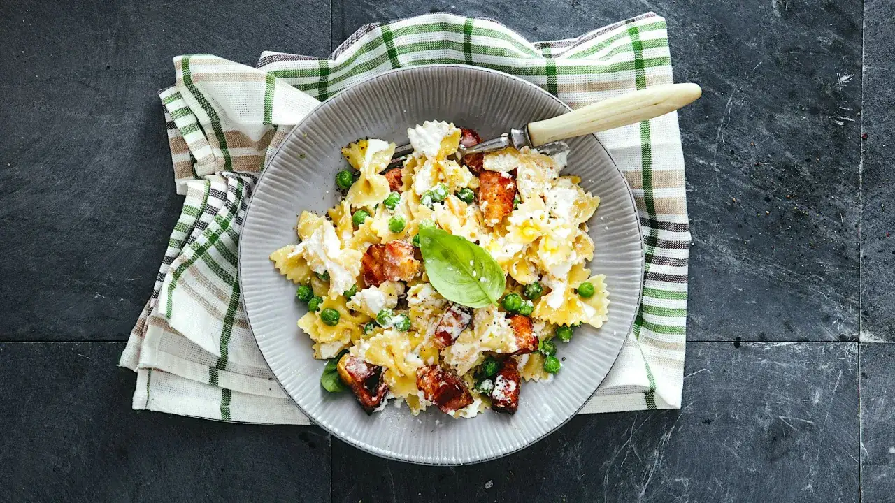 Farfalle con piselli, cubetti di salmone affumicato e ricotta cremosa, guarnite con basilico fresco.