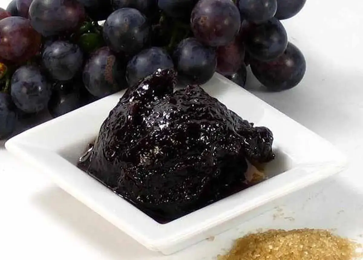 Marmellata di uva scura, perfetta per la cugn&agrave; ricetta. Accanto, un grappolo d'uva e zucchero di canna.