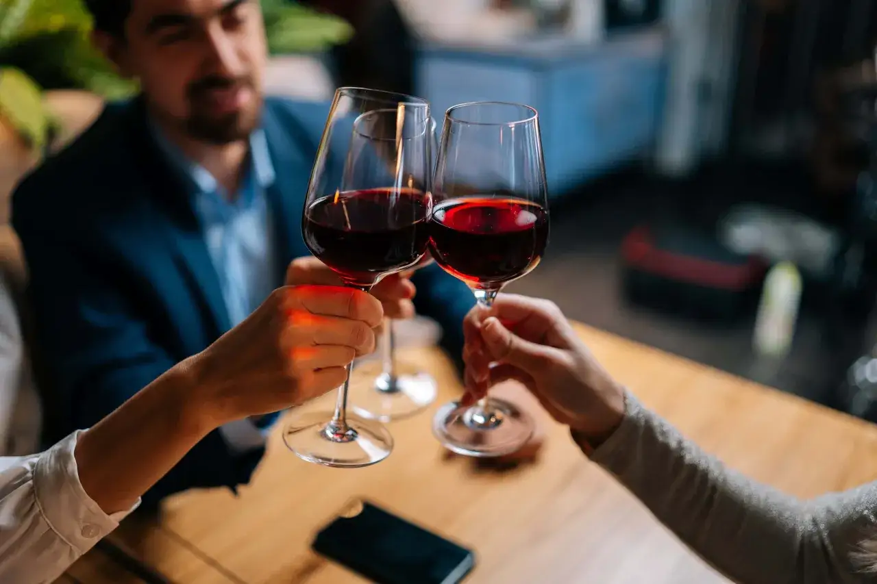 Brindisi con vino rosso: si tiene il calice per lo stelo, evitando di scaldare la bevanda. Un uomo e due donne festeggiano.