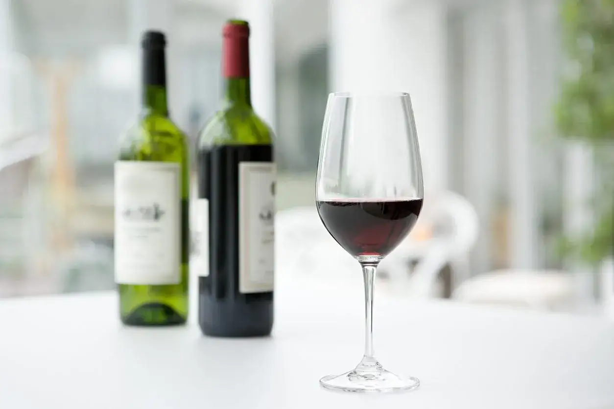 Un bicchiere di vino rosso, con due bottiglie sullo sfondo. Il vino scade, ma questo sembra ancora perfetto.
