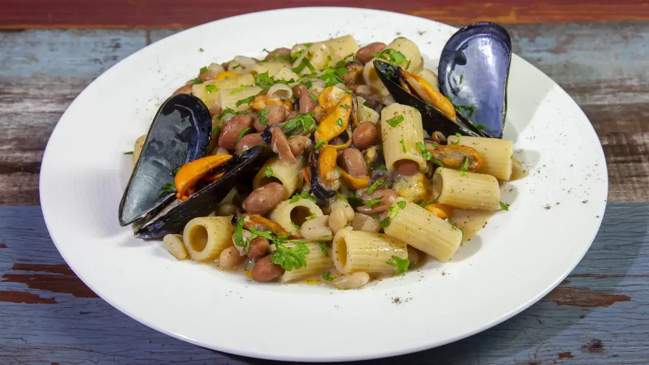 Piatto di pasta fagioli e cozze, un classico saporito, con rigatoni, fagioli borlotti e cannellini, e cozze nere aperte, guarnito con prezzemolo fresco.