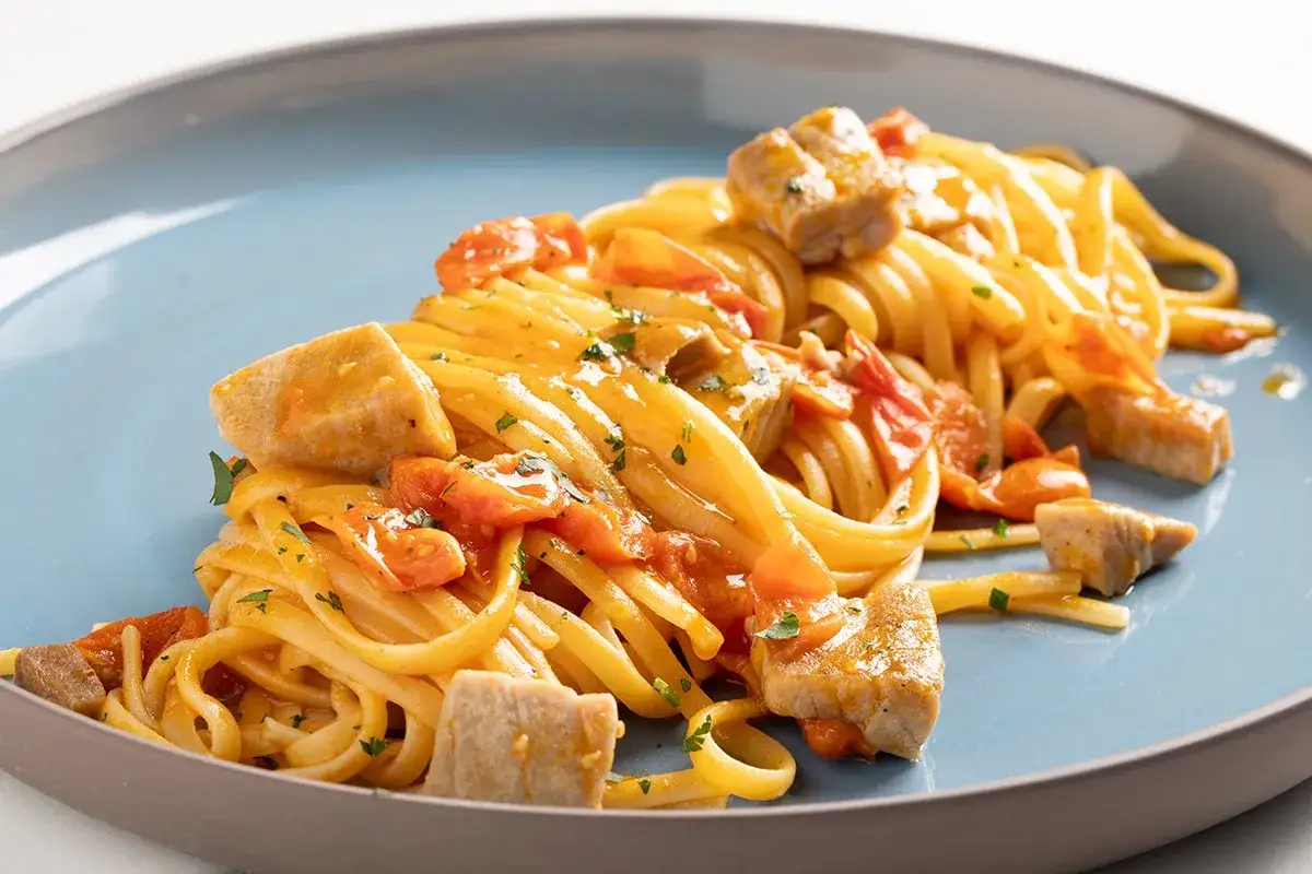 Un piatto invitante di pasta con tonno fresco, pomodorini e prezzemolo, servito su un piatto blu.