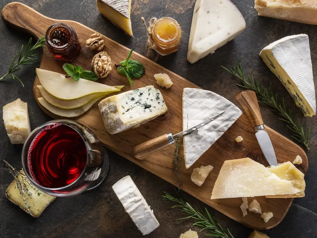 Un tagliere con vari formaggi, tra cui pecorino, pere, noci e un bicchiere di vino rosso.