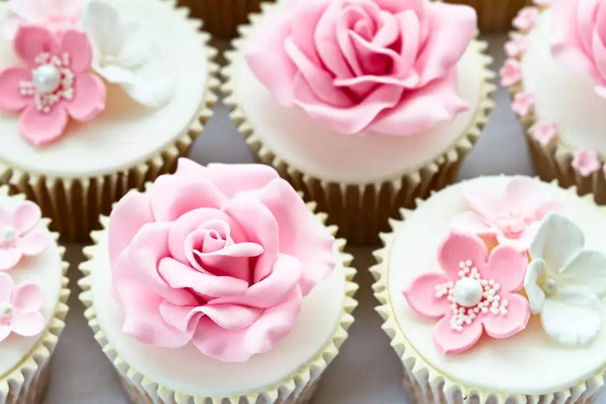 Cupcake decorati con rose e fiori in pasta di zucchero rosa e bianchi, perfetti per un'occasione speciale.