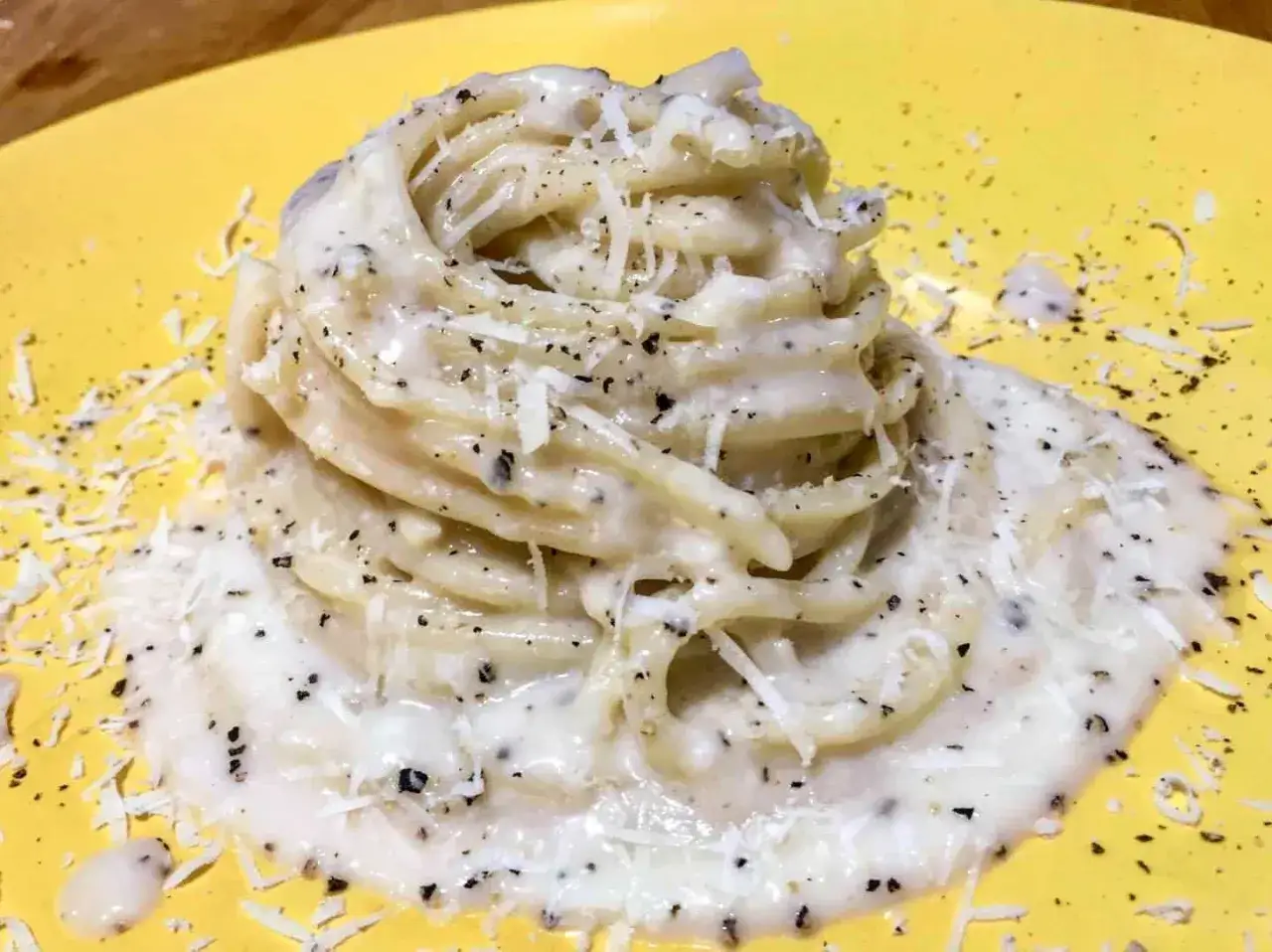 Un piatto di spaghetti al cacio e pepe, cremosi e ricchi di pecorino e pepe nero, serviti su un piatto giallo.