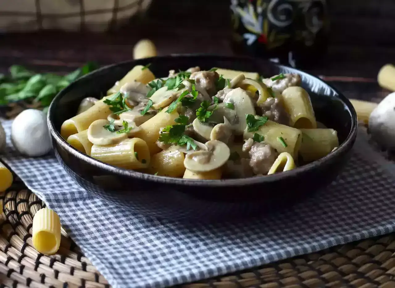 Piatto fumante di pasta salsiccia e funghi, guarnito con prezzemolo fresco.
