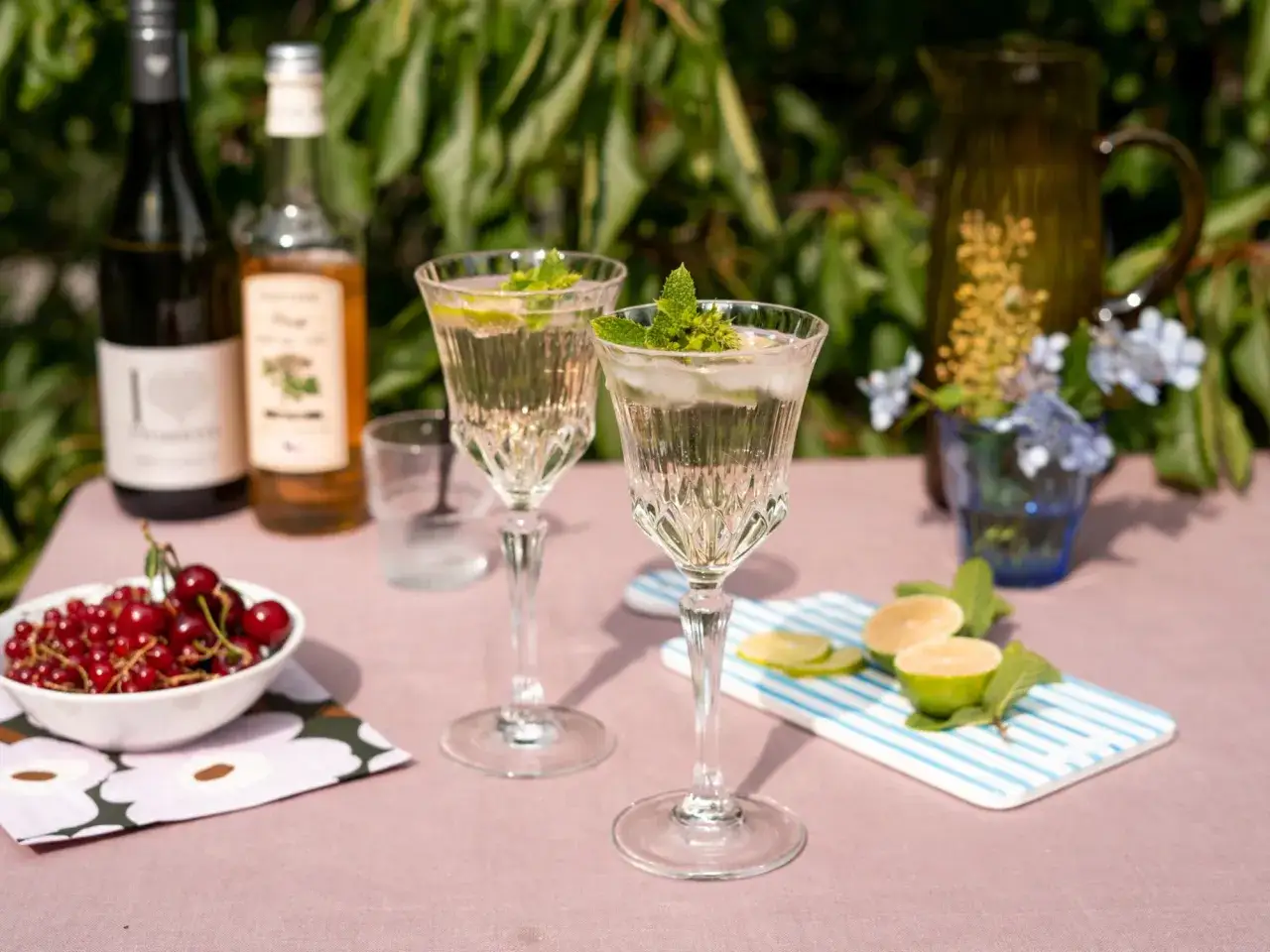 Un rinfrescante aperitivo con frutta, due bicchieri di cristallo con ghiaccio, menta e lime, accompagnati da una ciotola di ciliegie rosse e ribes.