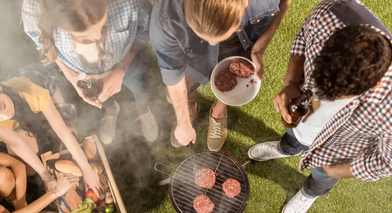 Amici preparano hamburger sulla griglia, con tanta carbonella per una grigliata perfetta.