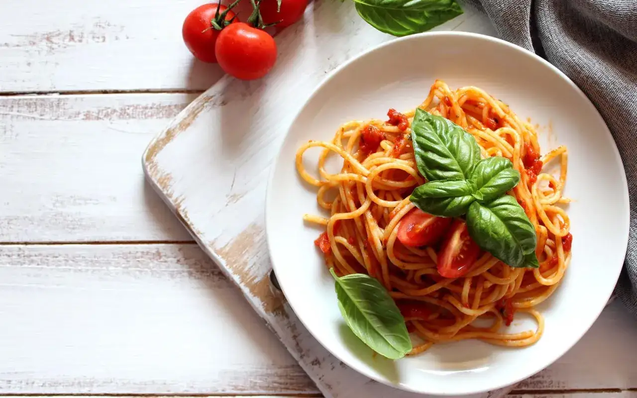 Spaghetti al sugo di pomodoro fresco, guarniti con basilico e pomodorini, su un piatto bianco.