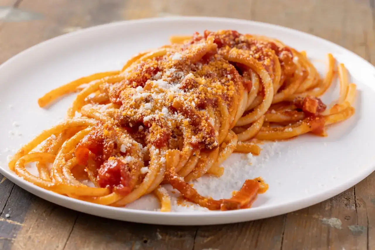 Un piatto di bucatini all'amatriciana ricetta, conditi con sugo rosso e abbondante pecorino grattugiato.