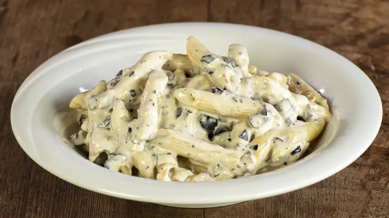 Penne cremose con pezzetti scuri, un piatto invitante di pasta alla cenere, servito in una ciotola bianca su un tavolo di legno.