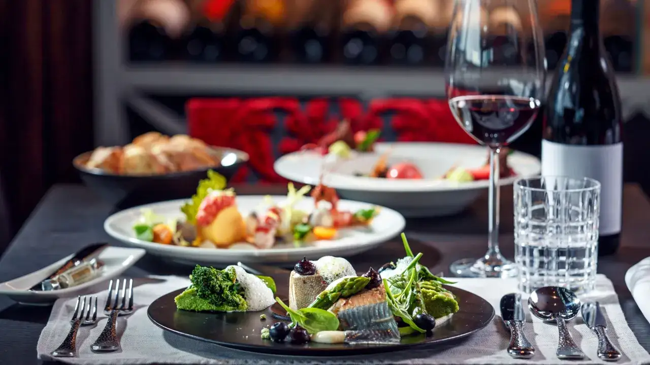 Un bicchiere di vino rosso accompagna un piatto di pesce finemente preparato, con contorni verdi e olive.