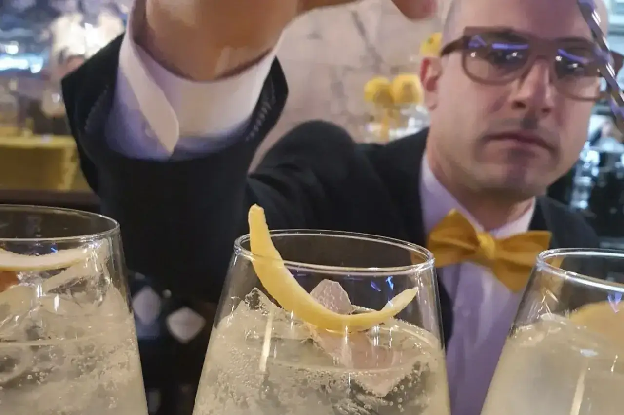 Un barista con papillon giallo prepara un bergamotto spritz, guarnito con scorza di limone e ghiaccio.