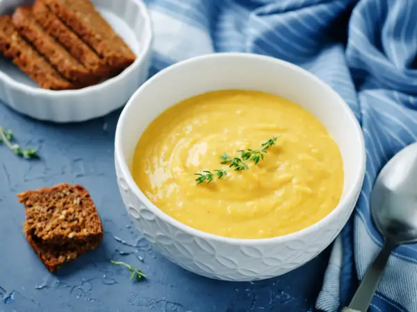 Una ciotola di cremosa salsa di ceci, guarnita con timo, accanto a fette di pane integrale e un tovagliolo blu a righe.