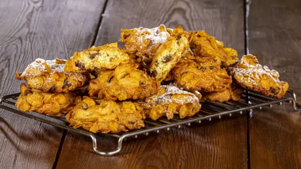 Un mucchio di croccanti biscotti alle corn flakes e uvetta, spolverati di zucchero a velo, sembrano piccole rose del deserto su una griglia.