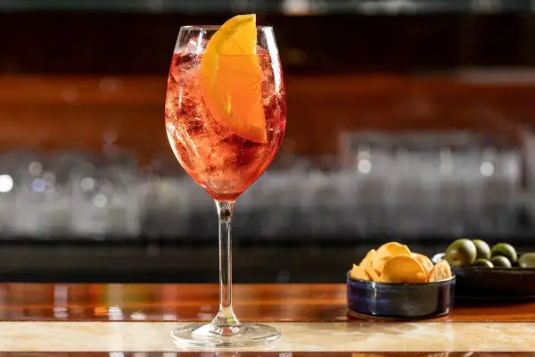 Un rinfrescante cocktail spritz, con una fetta d'arancia e ghiaccio, servito su un bancone di legno lucido.