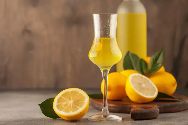 Un bicchiere di limoncello, frutto di un processo di limoncello scientifico, con limoni freschi e una bottiglia sullo sfondo.