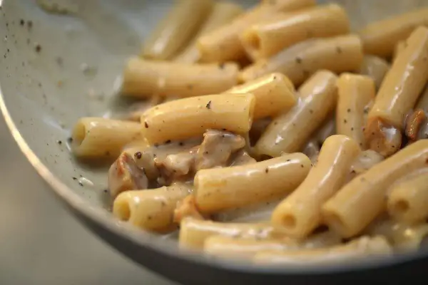 Primo piatto di pasta con guanciale croccante e crema al pecorino romano, un classico saporito.